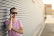 © Martin - Portrait of young handsome smiling man standing next to corrugated iron wall with modern designed smartphone in hand. Nice summer sunny weather and warm colors photo.