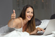 Woman using a laptop on the bed with thumbs up