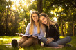 © Sunrise Team - Young beautiful ladies students sitting in the park outdoors on grass holding copybook doing homework.