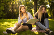 © Sunrise Team - Displeased young beautiful ladies students sitting in the park outdoors on grass holding copybook doing homework.