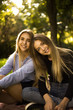 © Sunrise Team - Cheerful smiling girls sisters students sitting in the park outdoors on grass looking camera hugging.