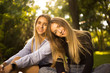 © Sunrise Team - Cheerful smiling girls sisters students sitting in the park outdoors on grass looking camera hugging.