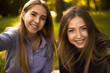 © Sunrise Team - Happy laughing girls sisters students sitting in the park outdoors on grass have a rest take a selfie by camera.