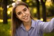 © Sunrise Team - Cheerful smiling girl student sitting in the park outdoors on grass have a rest take a selfie by camera.