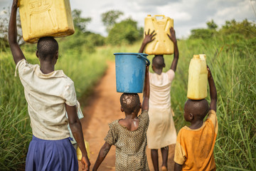 group of young african kids walking with buckets and jerrycans on their head as they prepare to brin