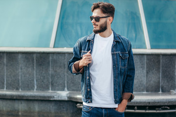 Wall Mural - A stylish man with a beard in glasses with a white T-shirt. Street photo