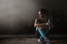 Female Runner Sitting Legs Crossed On Floor Holding Water Bottle