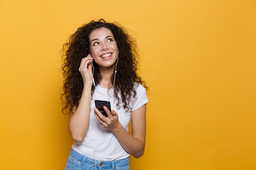 Sticker - Image of european woman 20s with curly hair holding cell phone and listening to music via earphones, isolated over yellow background