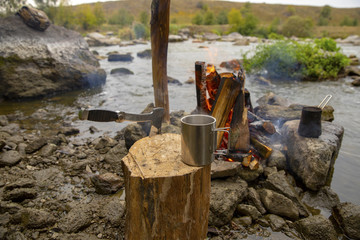 Aromatic and hot coffee on the fire. Bonfire and thermo mugs. Bonfire on the river bank.