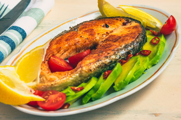 Roasted salmon steak on a plate with avocado and lemon close-up