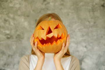 Wall Mural - Portrait of young skinny woman covering head by holding Jack O Lantern pumpkin against her face. All hallows eve Halloween party concept. Traditional decoration. Close up, copy space, background.