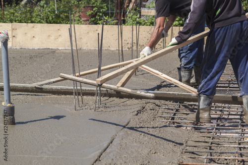 Two Workers Leveling Fresh Concrete Slab With A Special Wooden