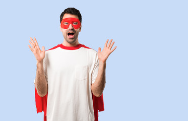 Superhero man with mask and red cape with surprise and shocked facial expression. Mouth open because not expect what has happened on isolated blue background