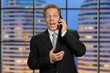 © DenisProduction.com - Cheerful businessman talking on mobile phone. Excited mature man in business suit talking on phone at evening office. Concept of business conversation.