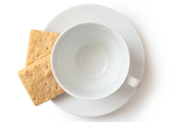 Wall Mural - An empty white ceramic cup and saucer with two square shortbread biscuits isolated on white from above.