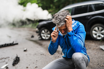 Wall Mural - Mature man making a phone call after a car accident, smoke in the background.