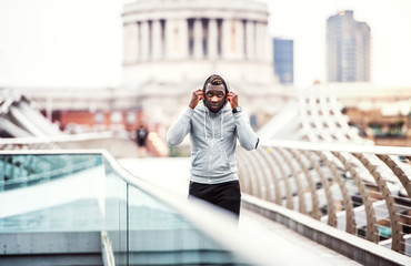 Poster - Black man runner with smartphone in an armband on the bridge in a city, resting.