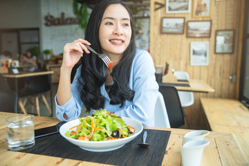 Happy woman eating healthy salad sitting on the table . Beautiful girl eating healthy food. Diet and healthy food concept