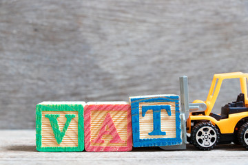 Sticker - Toy forklift hold color letter block T to complete word VAT (Abberviation of Value added tax) on wood background