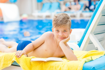 Wall Mural - Happy little boy is reading a book by the pool.  Relaxation resting vacations concept