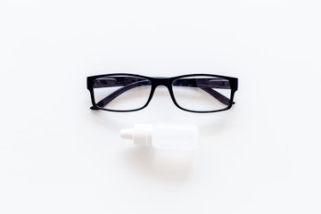 Eye health. Glasses with transparent optical lenses and eye drops on white background top view copy space closeup