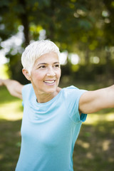 Wall Mural - Senior woman exercising tretching arm in the park