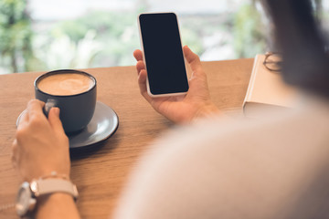 partial view of woman with coffee cup using smartphone at table in cafe