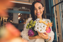 Portrait Of Smiling Young Woman Holding Colorful Bouquet From Various Flowers In Cafe