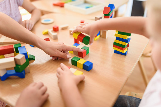 Preschool teacher with children playing with colorful wooden didactic toys at kindergarten