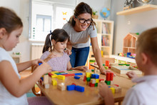 Preschool Teacher With Children Playing With Colorful Wooden Didactic Toys At Kindergarten
