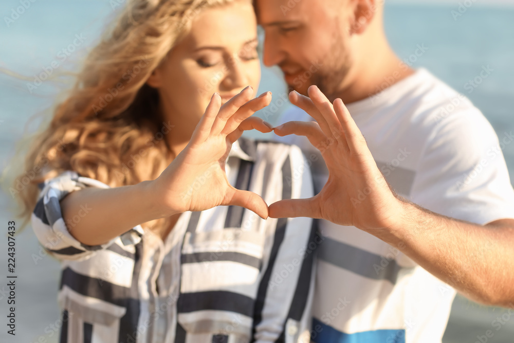 Cute young couple making heart with their hands on sea shore
