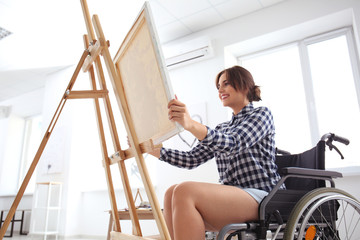 Young female artist in wheelchair painting picture at home