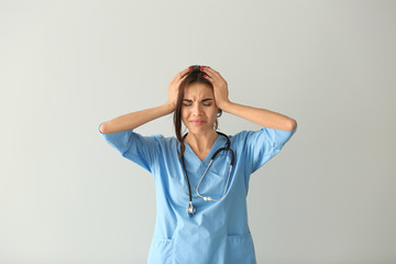 Wall Mural - Stressed female nurse on light background