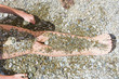 pair of female legs covered in pebbles on a beach near a sea