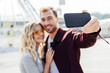 © LIGHTFIELD STUDIOS - selective focus of smiling couple in autumn outfit taking selfie with smartphone in city