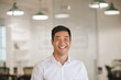 © mavoimages - Young Asian businessman laughing while standing in a modern office