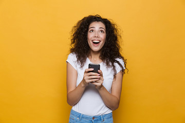 Wall Mural - Happy cute young woman posing isolated over yellow background using mobile phone.