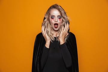 Sticker - Scary woman wearing black costume and halloween makeup looking at the camera, isolated over yellow background