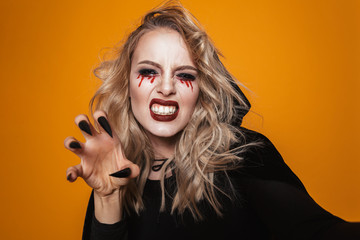 Poster - Terrifying woman wearing black costume and halloween makeup looking at the camera, isolated over yellow background