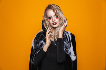 Poster - Scary wizard woman wearing black costume and halloween makeup looking at the camera, isolated over yellow background