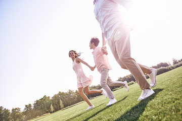 Family walk. Family of three running on grassy field smiling hap