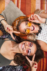 Photo from top of two joyful hippie girls, smiling and lying on blanket outdoor head to head