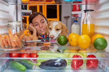 Woman and her dog in front of fridge late at night. Picture taken from the inside of frigde.