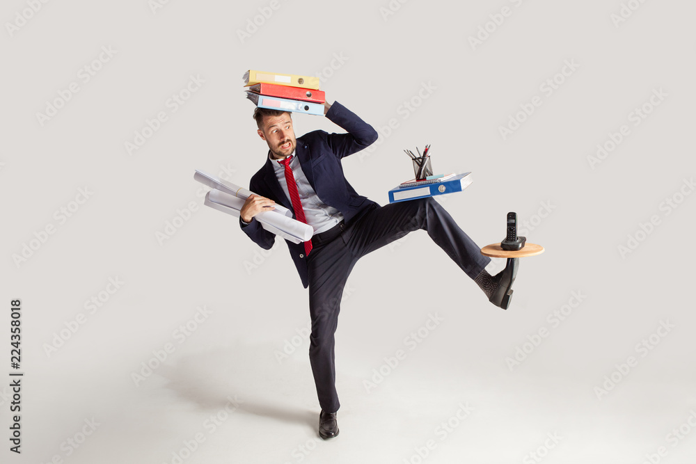 Young businessman in a suit juggling with office supplies in his office, isolated on white background. Conceptual collage with phone, folders. The business, office, work concept. - obrazy, fototapety, plakaty 