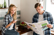 couple with smartphone and newspaper spending morning in kitchen at home