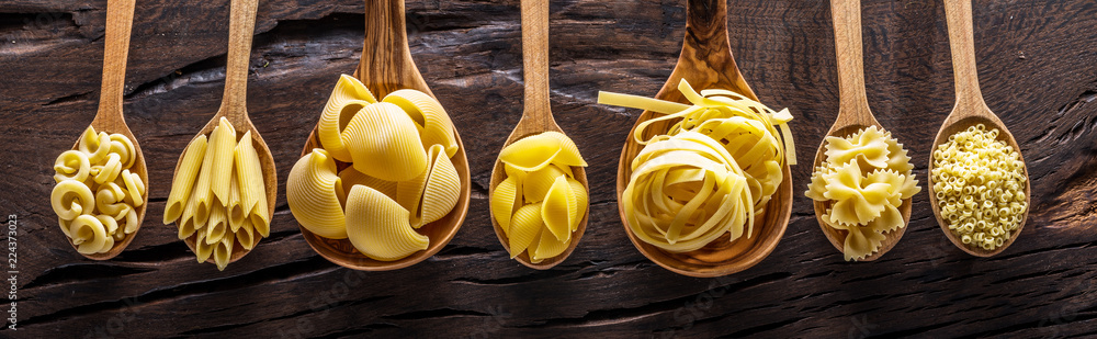 Different pasta types in wooden spoons on the table. Top view. - obrazy, fototapety, plakaty 