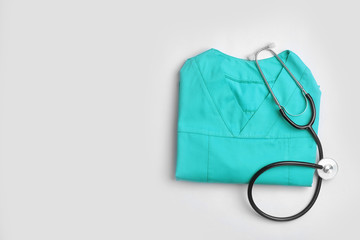 Folded medical uniform with stethoscope and space for text on white background, top view