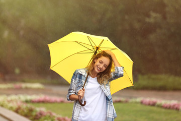 Wall Mural - Happy young woman with umbrella under rain in park