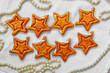 Two rows of eight decorative golden stars handmade from dough on a white fabric surface with pearl necklace