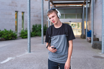 Wall Mural - Sad teenager standing in front of his school while listening to music with his headphones.